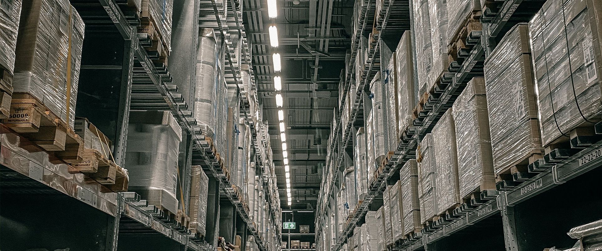 High-bay warehouse aisle of shrink-wrapped pallets, the kind of receiving floor shipping to Amazon FBA by LTL lands on