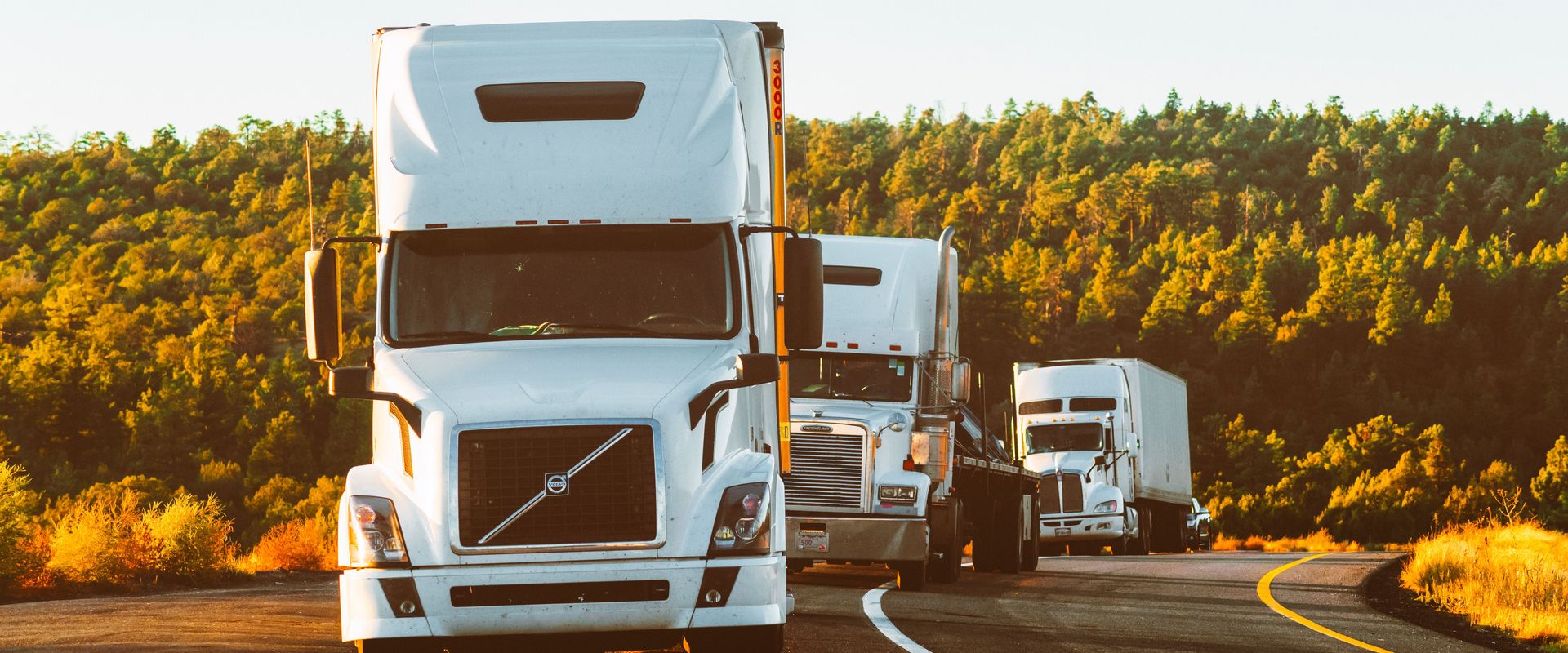 Three tractor-trailers on a highway at sunset: how is LTL freight priced depends on class, weight, and lanes like this