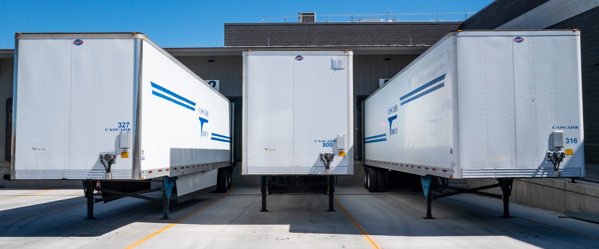 Three dry-van trailers backed into loading docks, the everyday equipment behind LTL and truckload freight services
